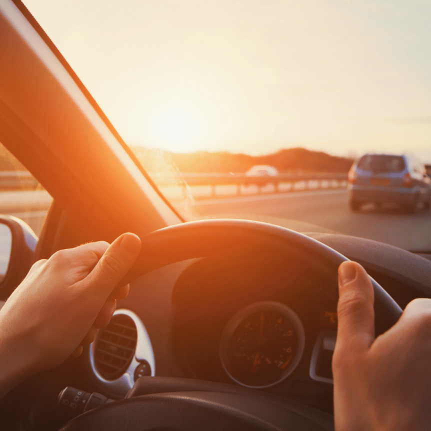 visual image of hands on steering wheel, driving on highway during sunset